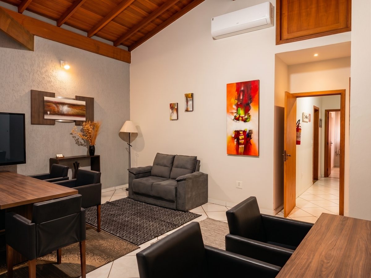 Sala de espera do escritório Martelo & Messas, com sofá, poltronas, obras de arte e teto de madeira aparente.